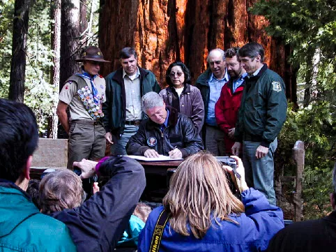 People gathered at Trail of a Hundred Giants, President Bill Clinton signing the Proclamation at a table.